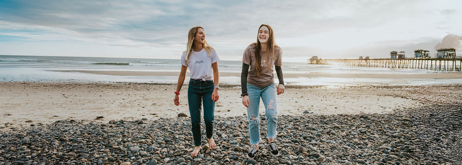 Two people walking on a beach with a pier in the background